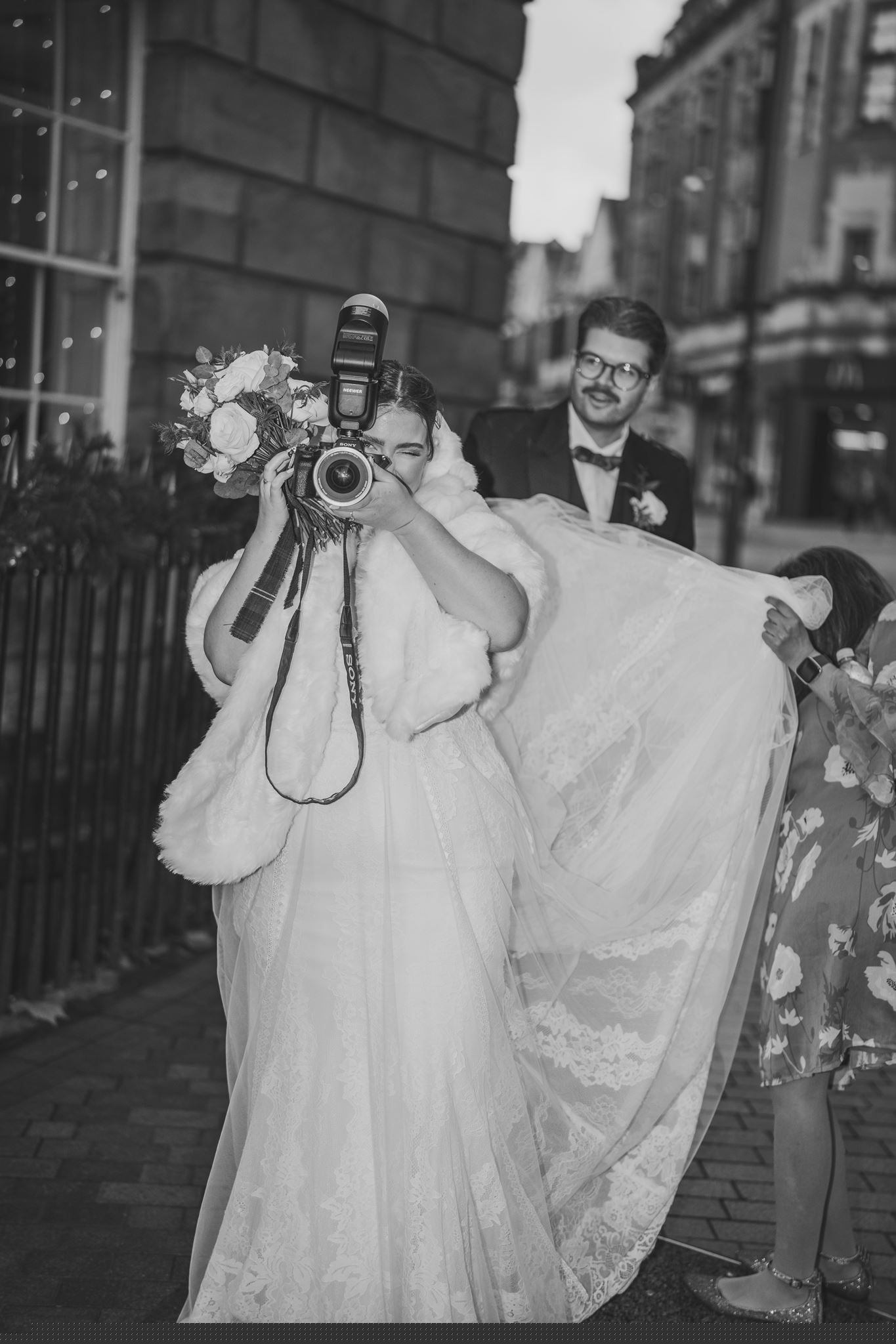 Bride playfully taking a photograph while her groom looks on
