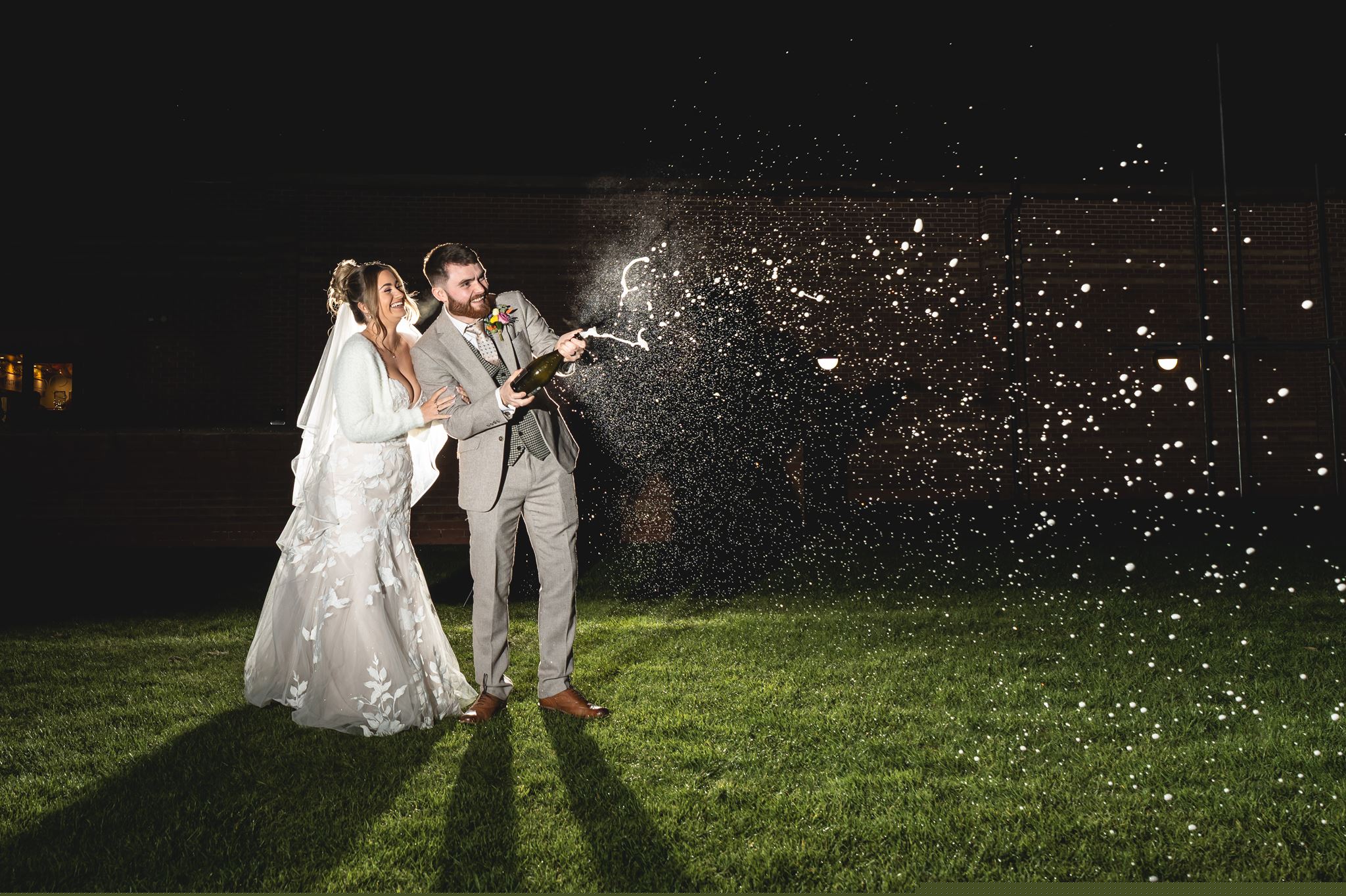 Newlyweds laughing as they spray champagne at night