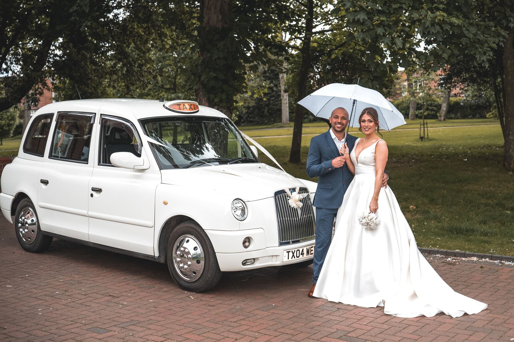 Bride and groom beneath an umbrella beside their wedding taxi