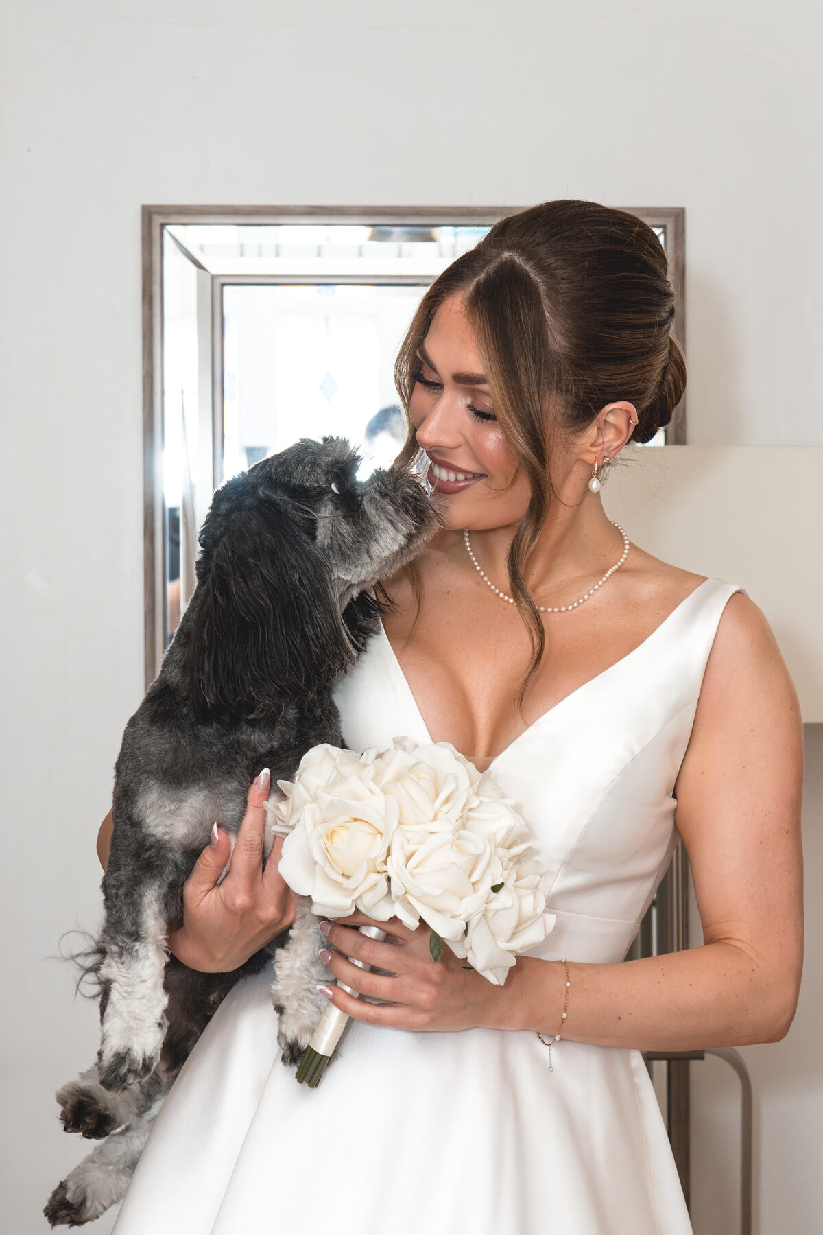 Bride smiling as her dog gives her a kiss