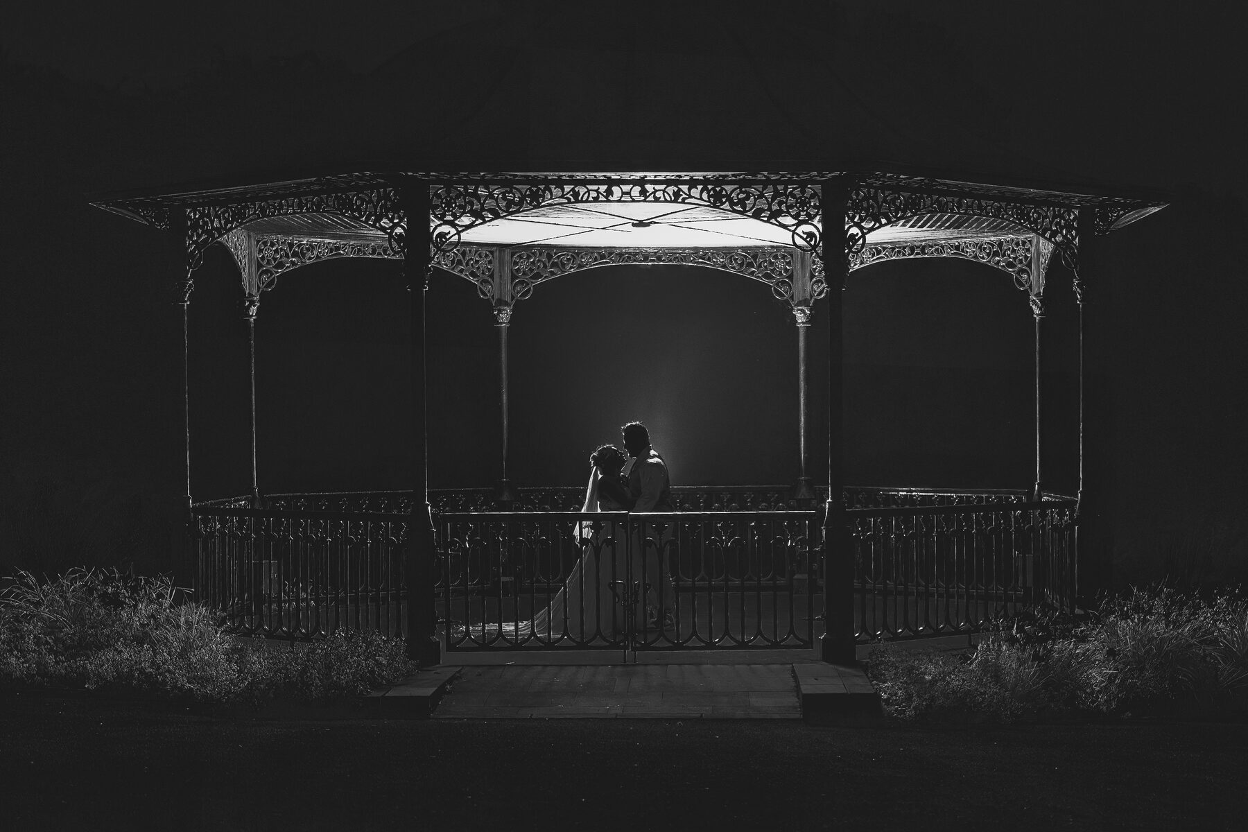 Black and white evening portrait of a couple beneath a gazebo